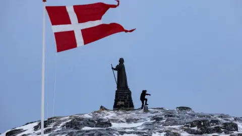 Danish flag flutters beside the Hans Egede statue in Nuuk, Greenland.