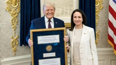 Donald Trump holds a Nobel Peace Prize medal as Maria Corina Machado stands beside him at the White House