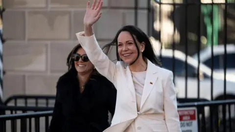 Maria Corina Machado waves in a white suit after leaving the White House