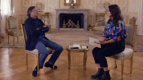Gustavo Petro and BBC journalist Ione Wells sit facing each other in an ornate room with parquet flooring and cream-colored walls with intricate moldings