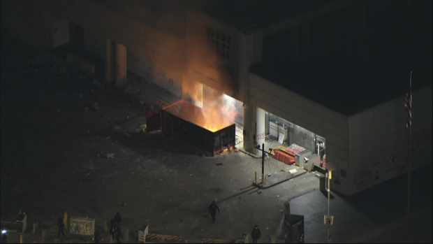 Small group sets a dumpster fire near the federal building's loading dock as firefighters are kept back.