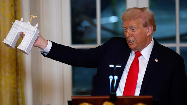 President Trump holds a model of an arch as he delivers remarks during a ballroom fundraising dinner in the East Room of the White House on Oct. 15, 2025.