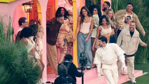 Celebrities gather on the porch of Bad Bunny's pink casita set as he dances in front