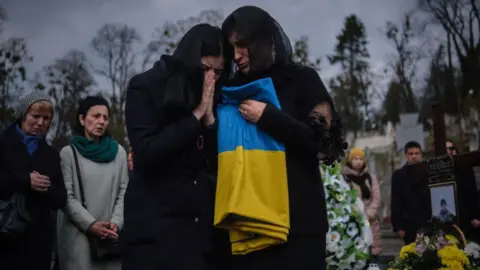 A mother embraces the Ukrainian flag at a funeral in Lviv, 2022