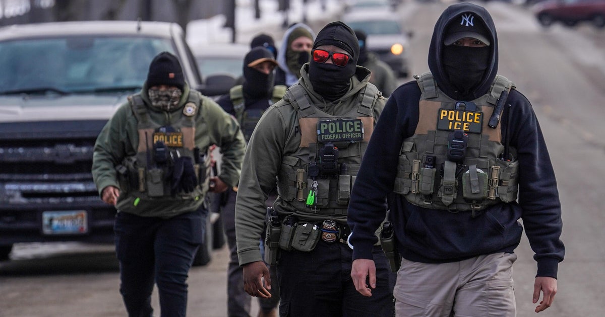 ICE officers walking near vehicles during an enforcement operation