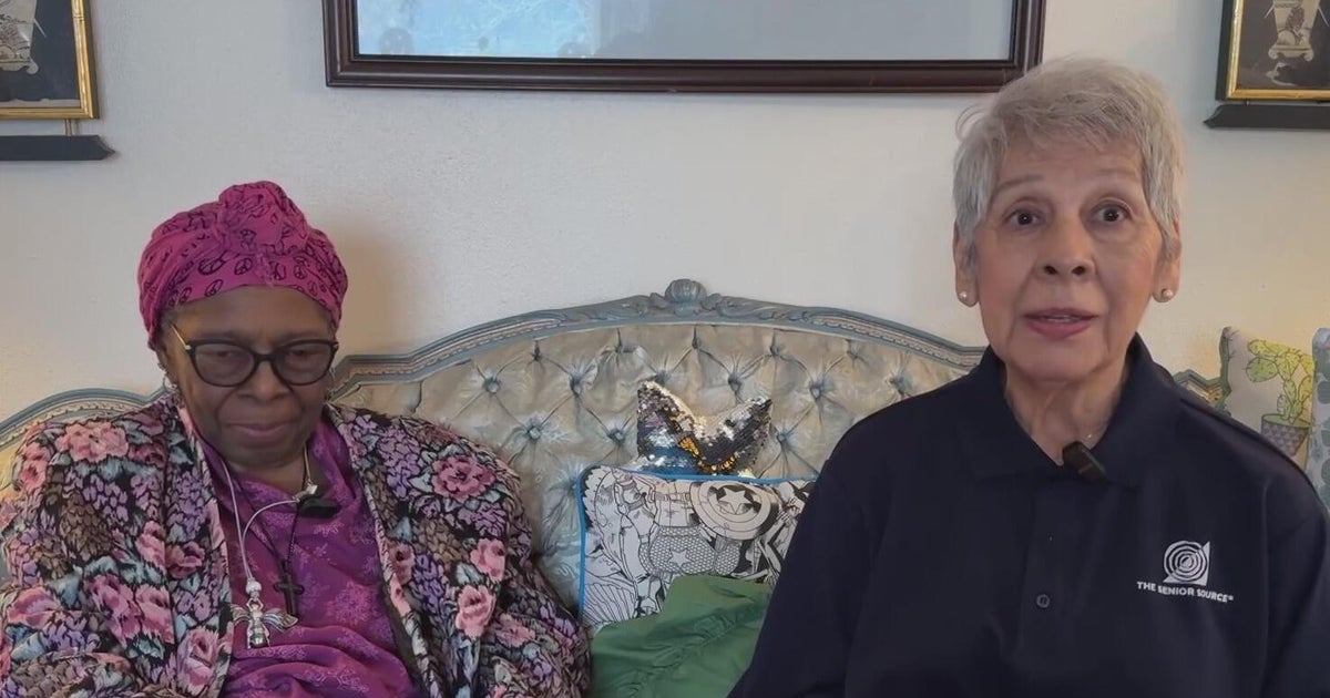 Two middle-aged women seated on a couch talking