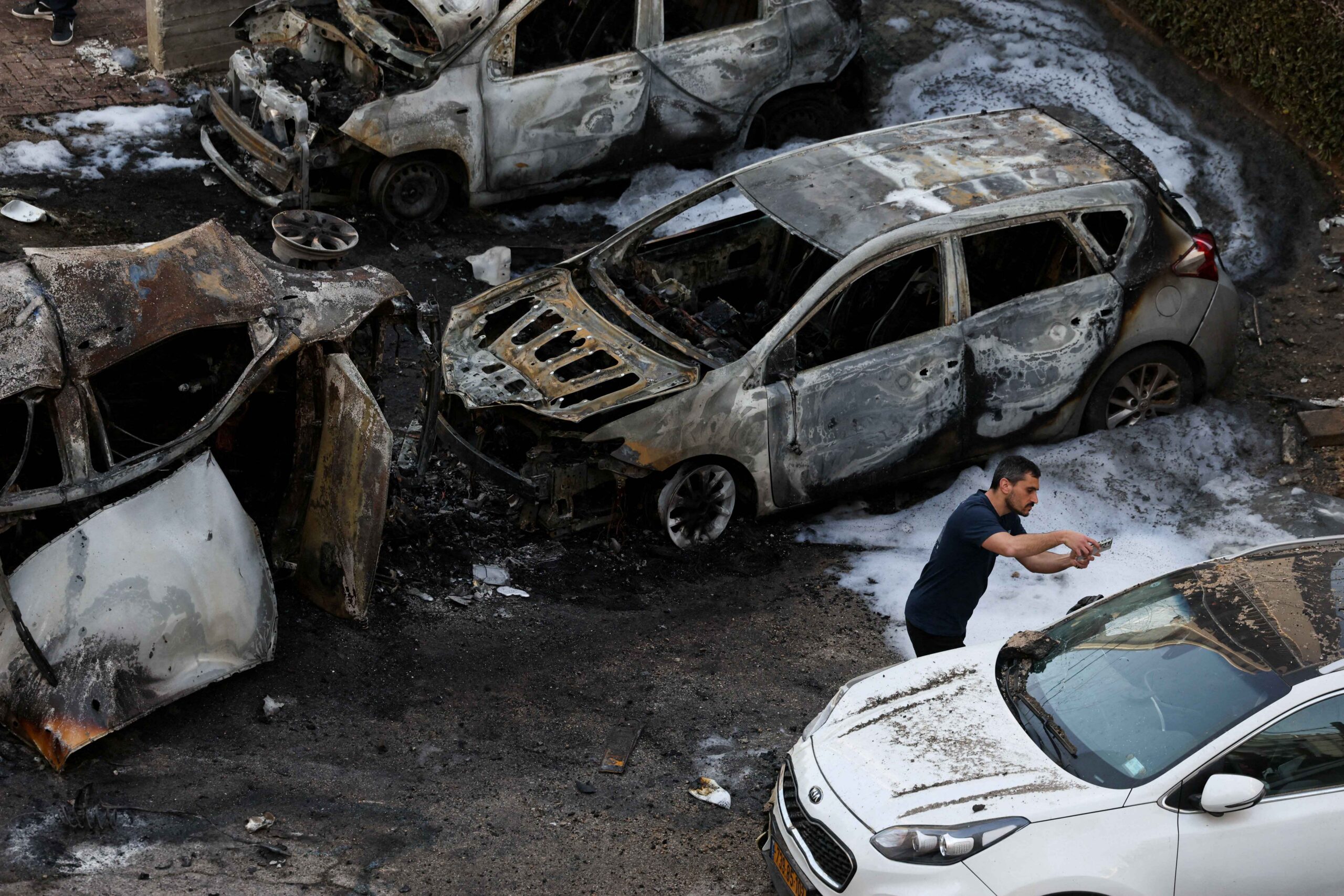 Aftermath of an explosion with burned vehicles and debris on a street