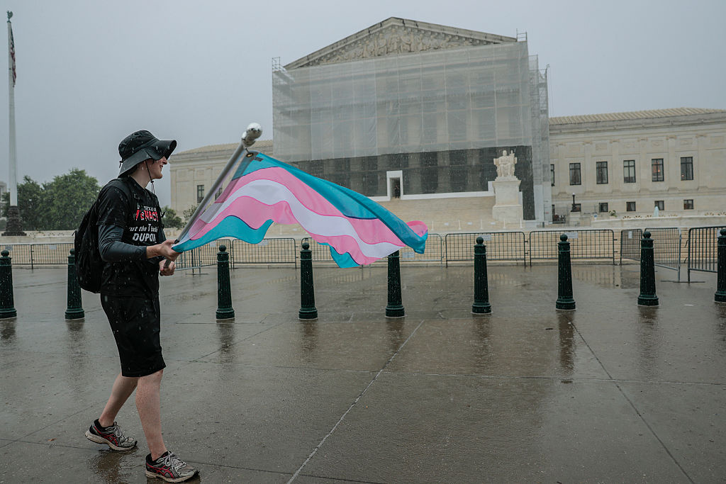 A protester with an American flag stands outside the U.S. Supreme Court in rainy weather.