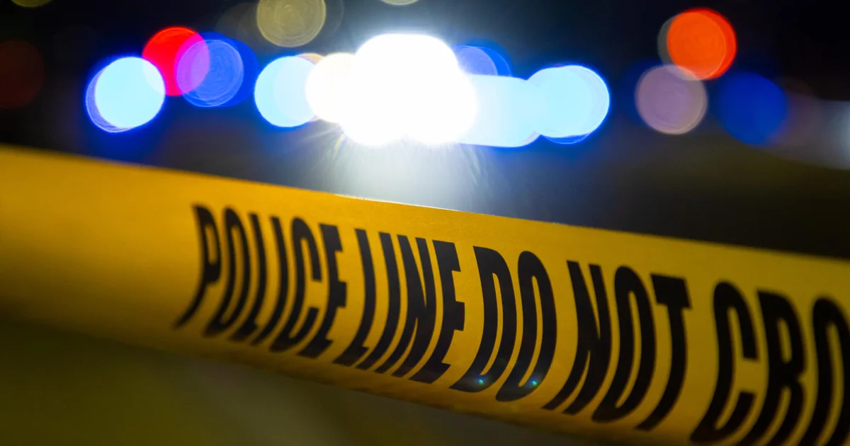 Police line tape with emergency lights blurred in the background.