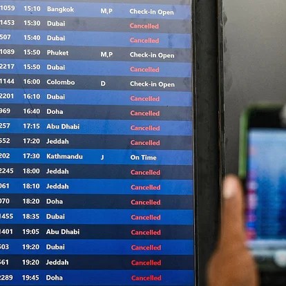 A passenger takes pictures of a flight information board at the Chhatrapati Shivaji Maharaj International Airport in Mumbai after airlines suspended flights to destinations in the Middle East. - Punit PARANJPE /AFP via Getty Images
