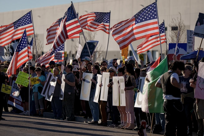 Protesters in Utah opposing the proposed ICE detention center at the warehouse, holding American flags and signs reading 'ICE OUT OF UTAH'.
